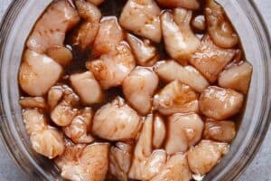 Chicken pieces marinating in soy sauce, egg, and Shaoxing wine in a glass bowl.