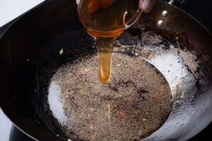 Honey being poured into a wok with simmering lemon sauce.