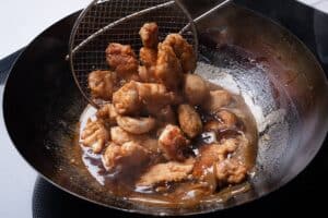 Crispy fried chicken being tossed through sticky lemon sauce in a wok.