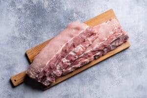 Raw baby back ribs sitting on a wooden cutting board.