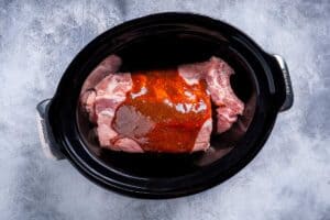 Baby back ribs inside a slow cooker with barbecue sauce mixture poured on top.