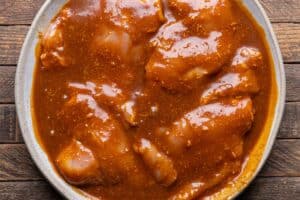 Chicken thighs coated in Thai satay marinade in a shallow bowl.
