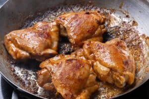 Chicken thighs browning in a skillet on the stovetop.