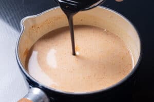 Peanut sauce simmering in a saucepan with sauce being poured in.