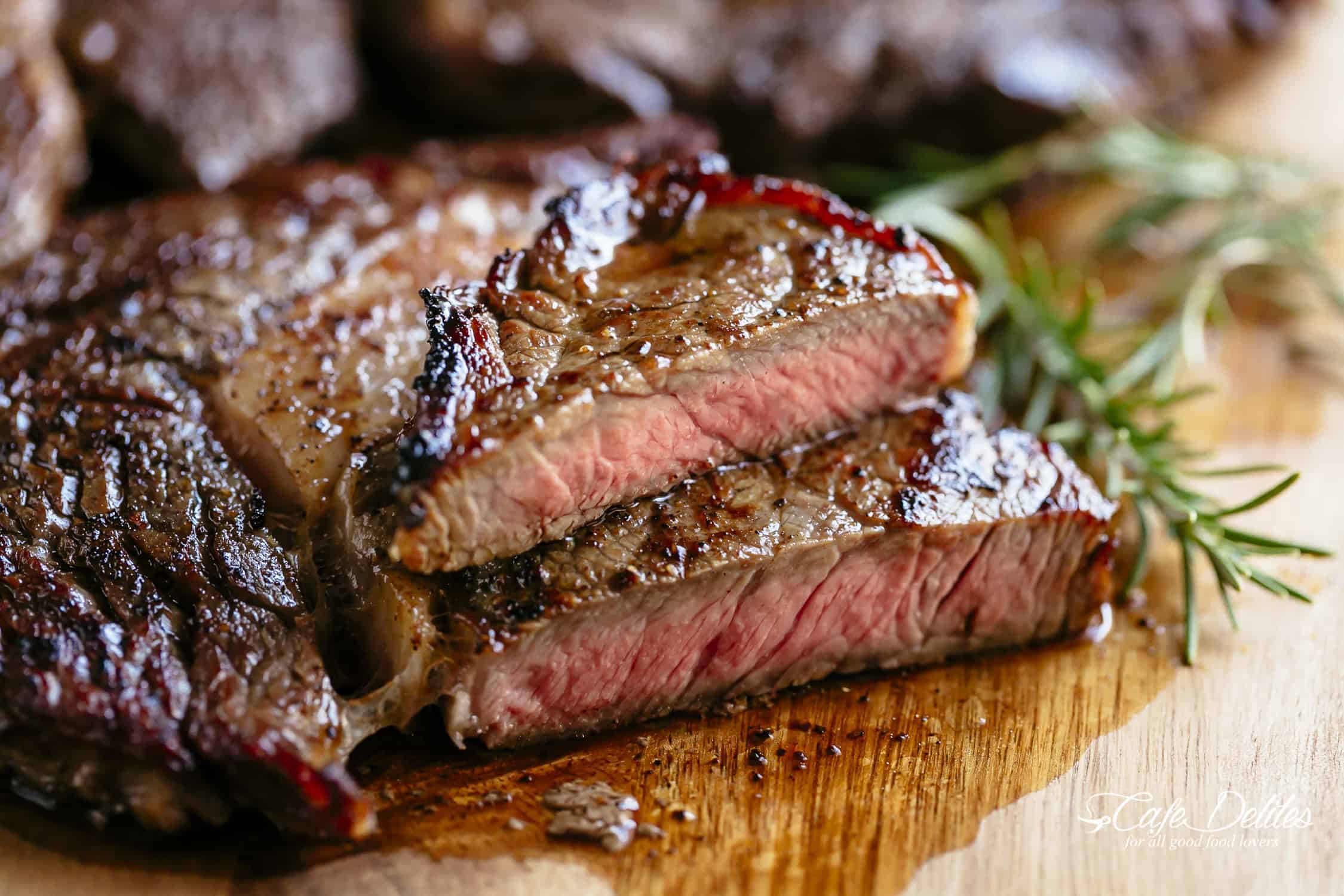 Side view of sliced, medium rare steak on a wood chopping board and a stick of rosemary.