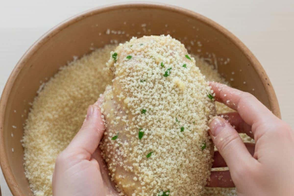 Dredging each marinated chicken piece in the crumb mixture.