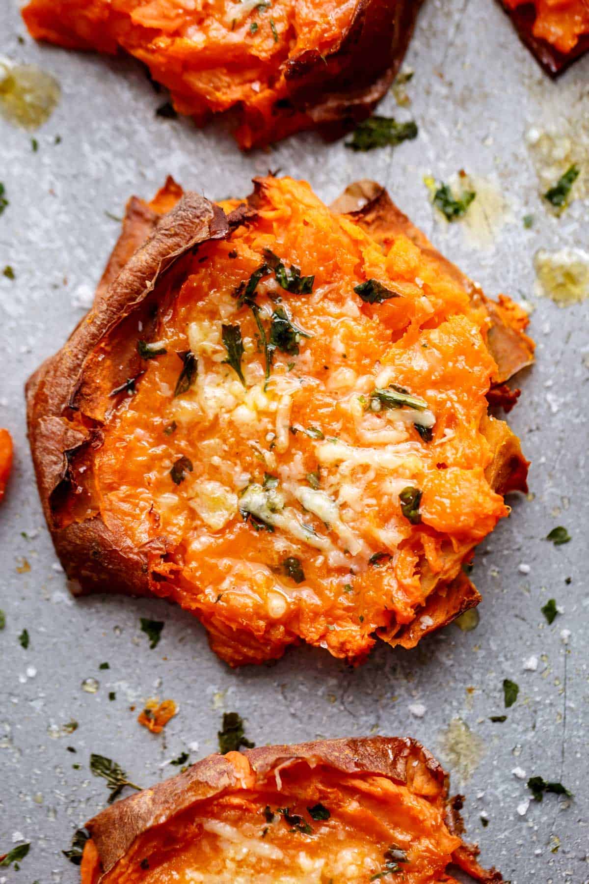Top view Image of a single slice of grilled, smashed sweet potato with parmesan and parsley.