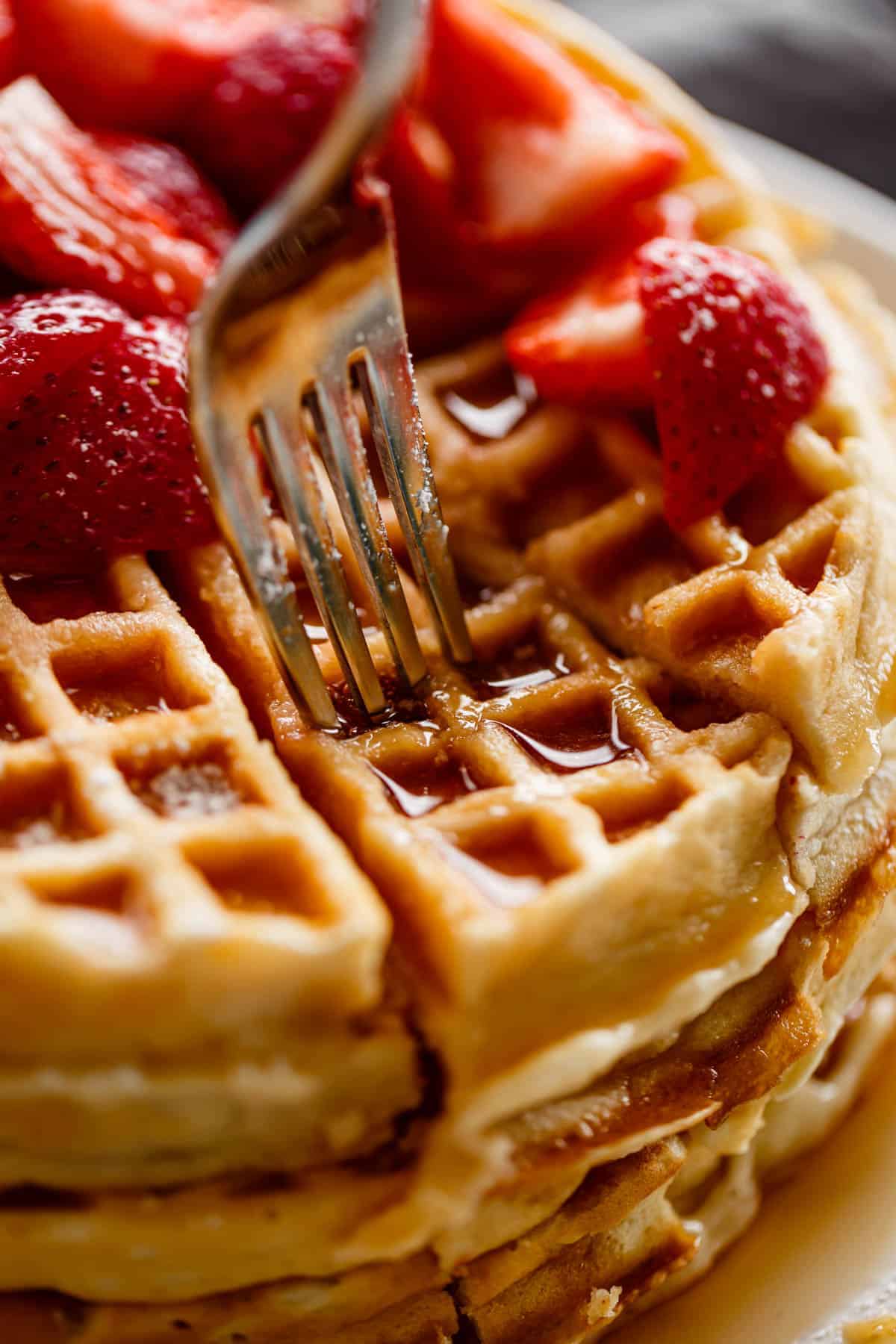 Homemade Belgian Waffles recipe fluffy waffles! | #belgiumwaffles #breakfast #easy #recipe Close up image of fork piercing a stack of waffles, drenched in maple syrup and covered with chopped strawberries.