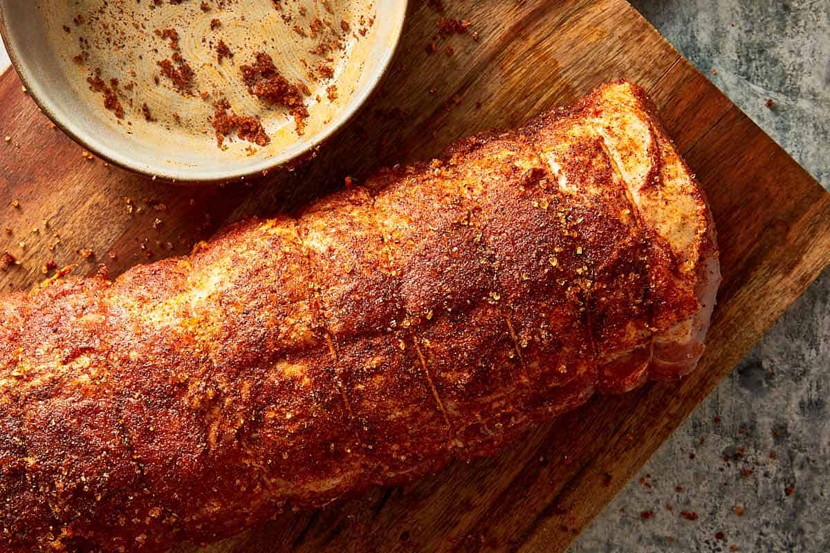 a seasoned pork loin resting on a board next to a plate with spice rub