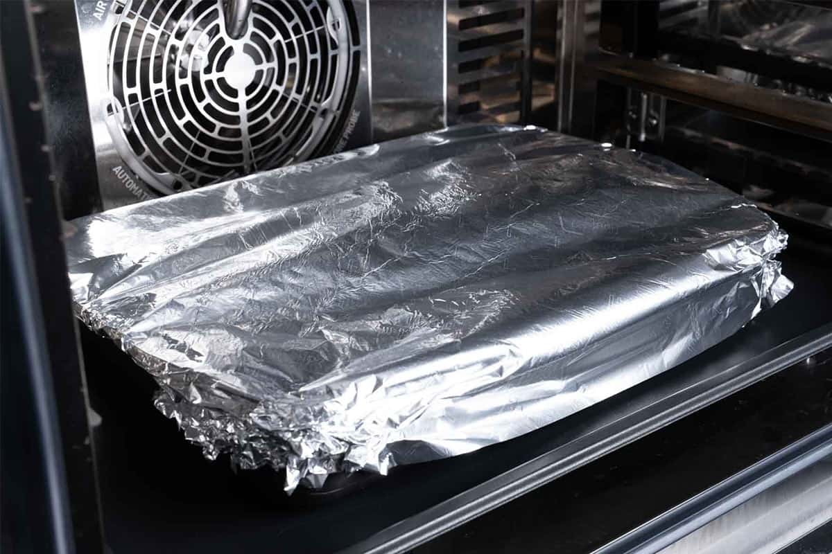 Image of the ribs being cooked in the oven covered with foil.