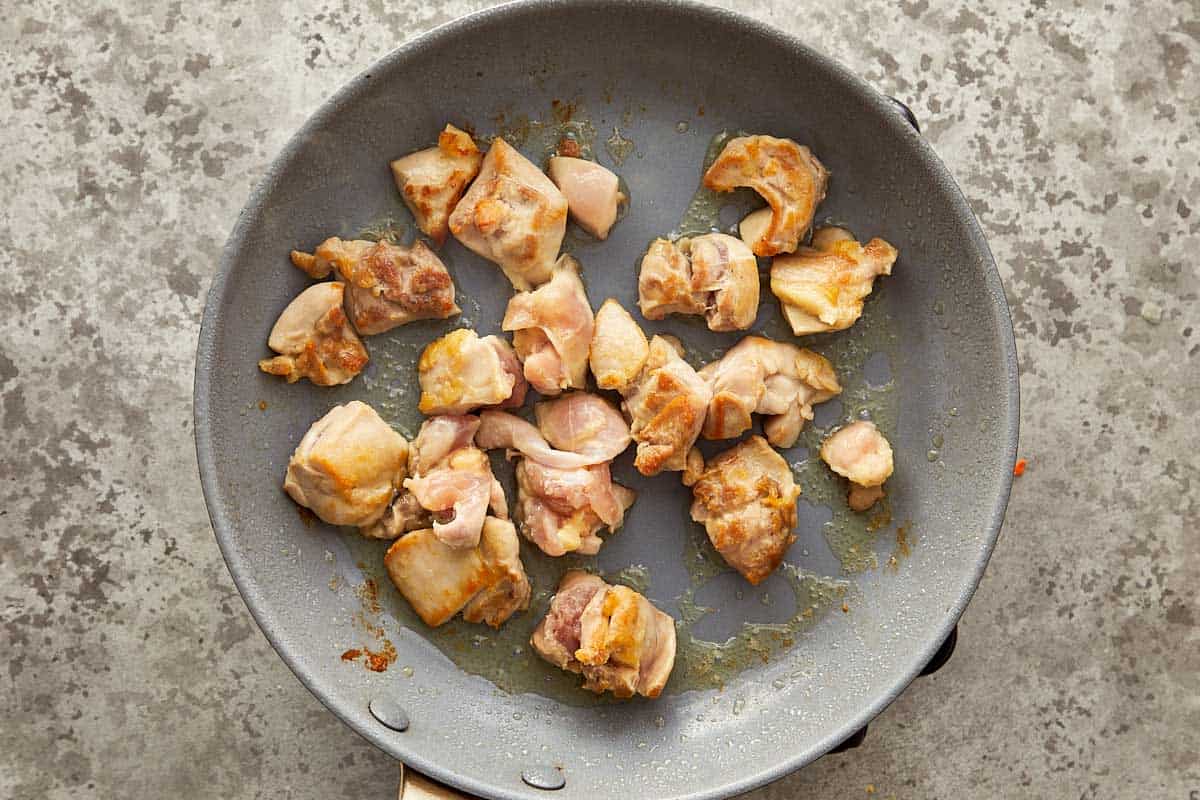 Chicken thighs browning in a skillet before adding to slow cooker chicken corn chowder.