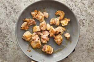 Chicken thighs browning in a skillet before adding to slow cooker chicken corn chowder.