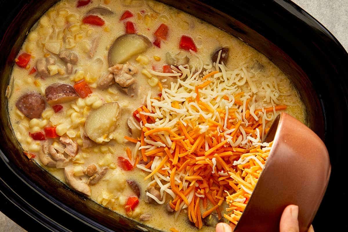 Cheddar and mozzarella cheese being stirred into creamy chicken bacon corn chowder.
