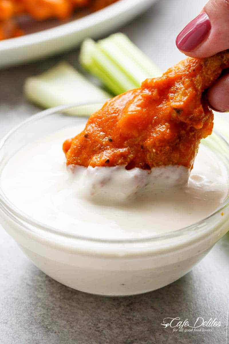 An image of a chicken wing covered in buffalo sauce being dipped into blue cheese sauce.