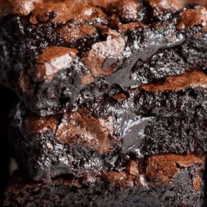 Side view of three slices of chocolate brownie stacked on top of each other. The brownies have a light brown top and dark, gooey interior.