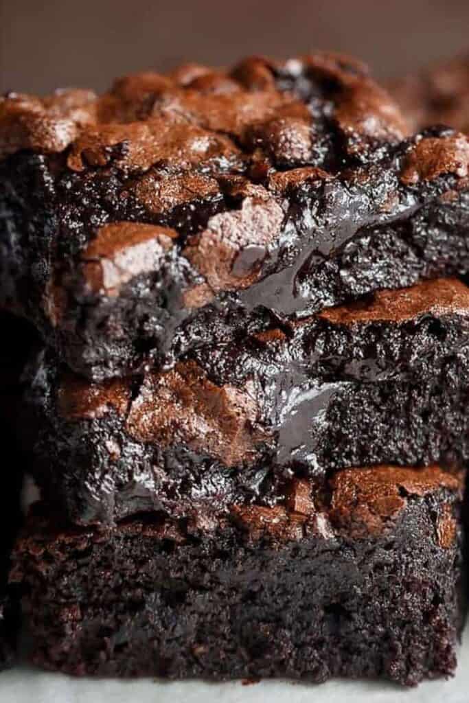 Side view of three slices of chocolate brownie stacked on top of each other. The brownies have a light brown top and dark, gooey interior.