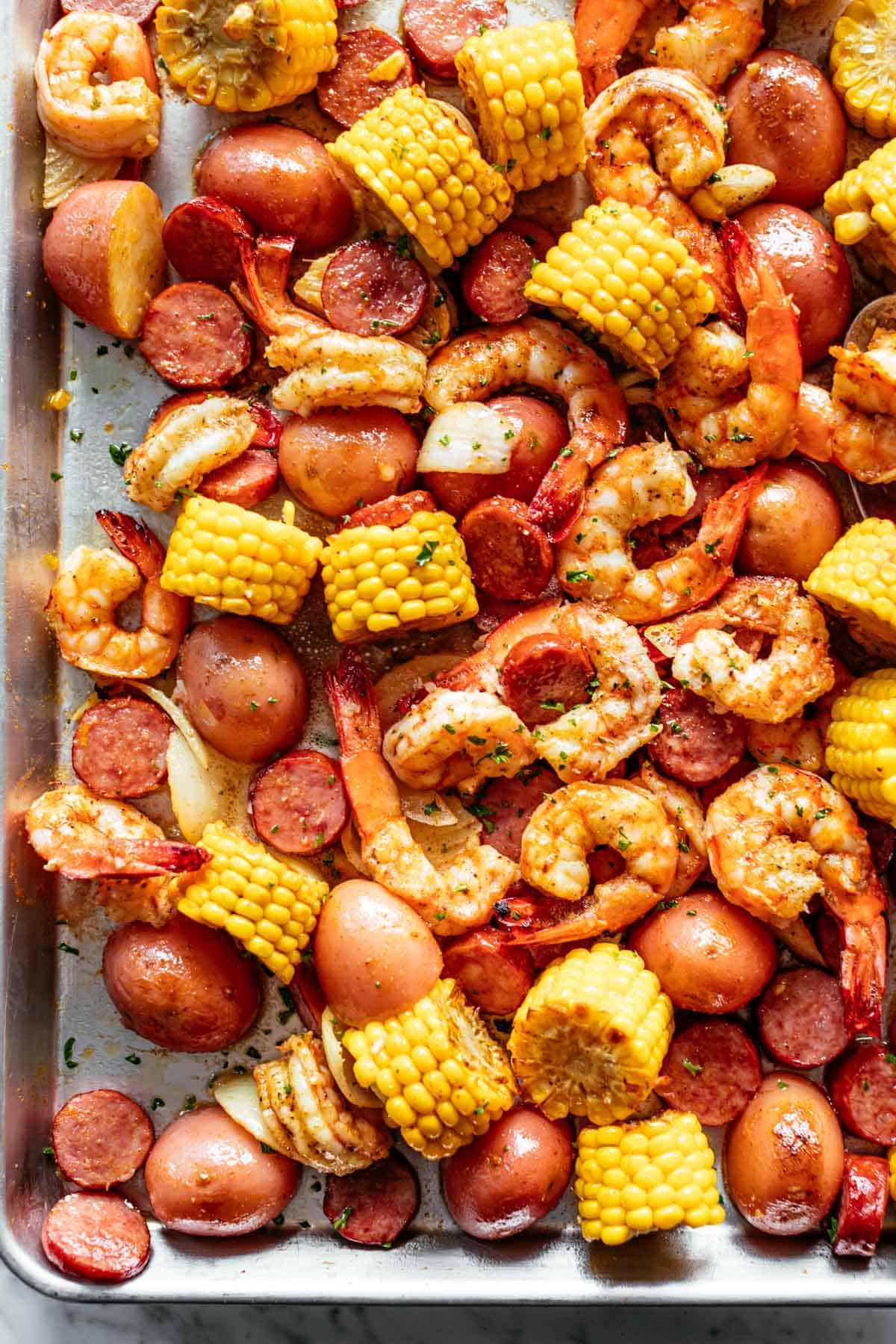 Shrimp Boil smothered in garlic butter mixture and Old Bay seasoning with chunks of red potatoes and corn on the cob on a silver tray.