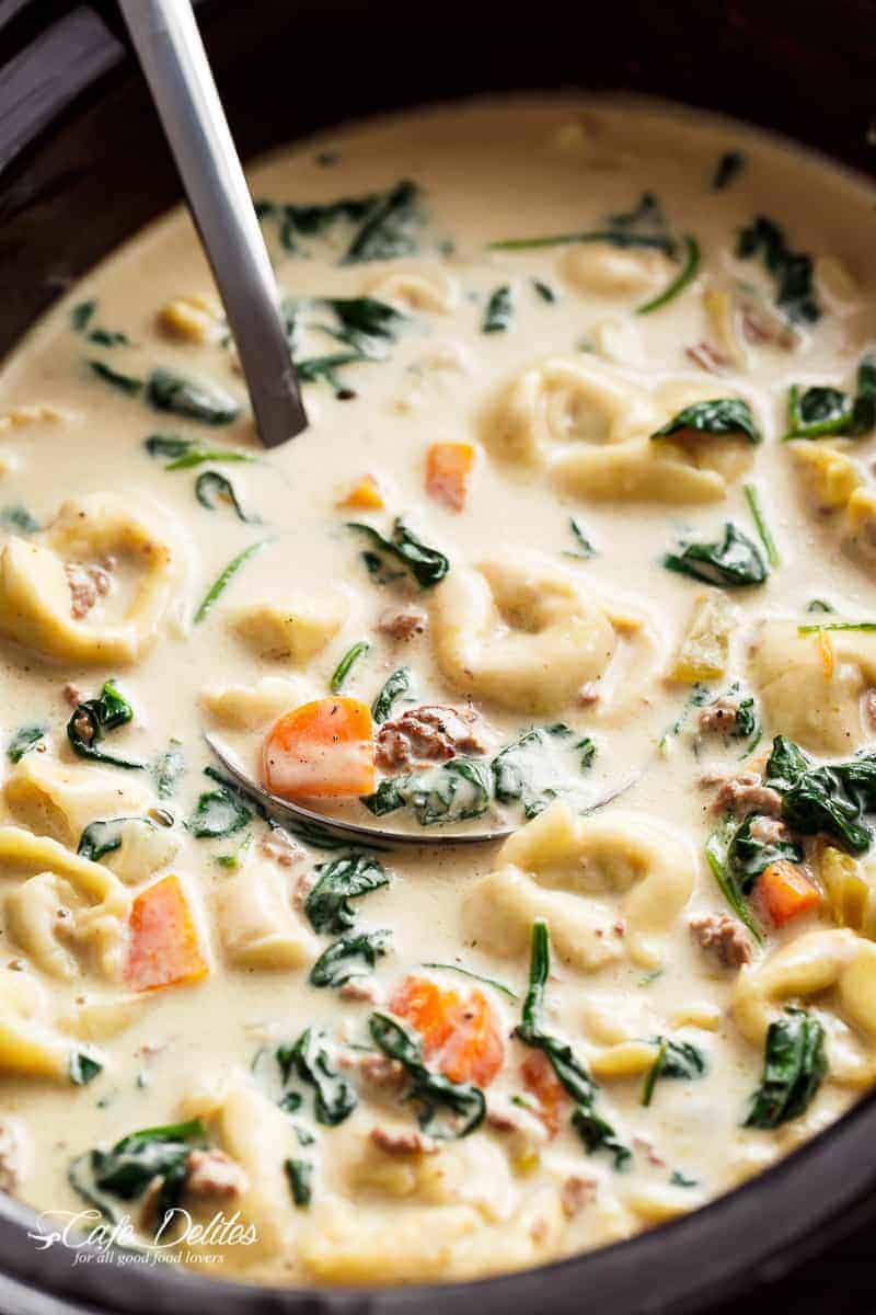 Close-up image of an iron ladle completely submerged in the rich and creamy tortellini soup.