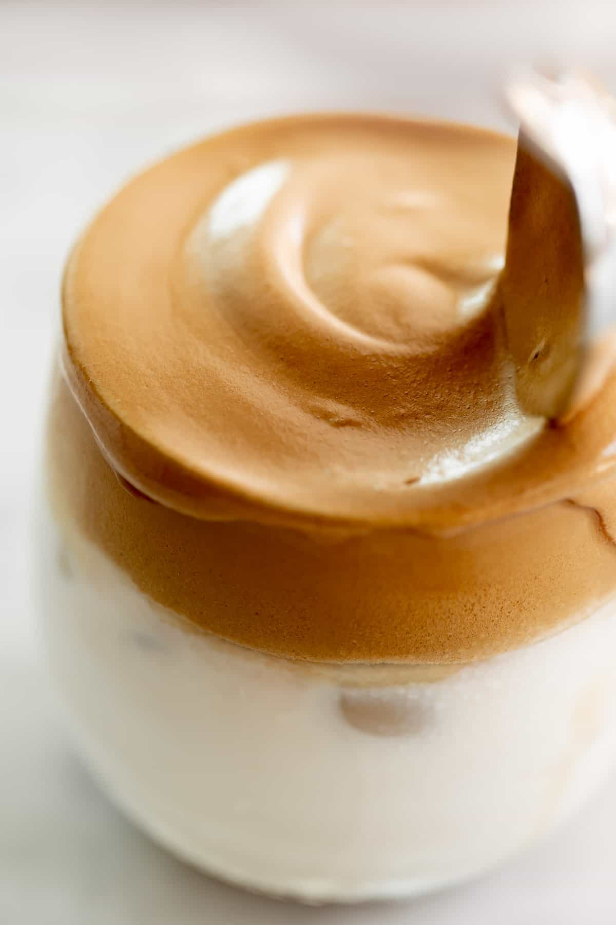 Whipped dalgona coffee on top of a glass full of milk. 