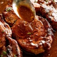 Zoom in image of a silver spoon pouring thin brown sauce over BBQ baked pork chops.
