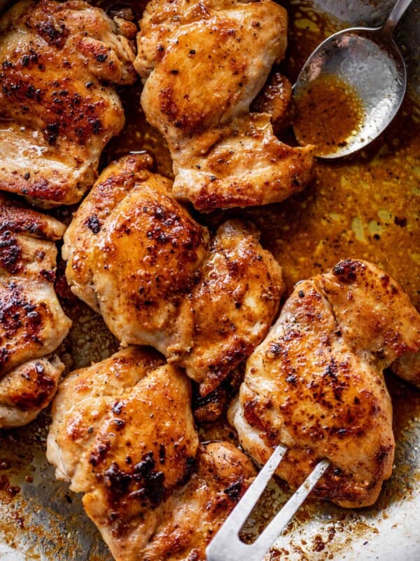 Crispy boneless chicken thighs in a silver pan, being picked up by a fork kitchen.