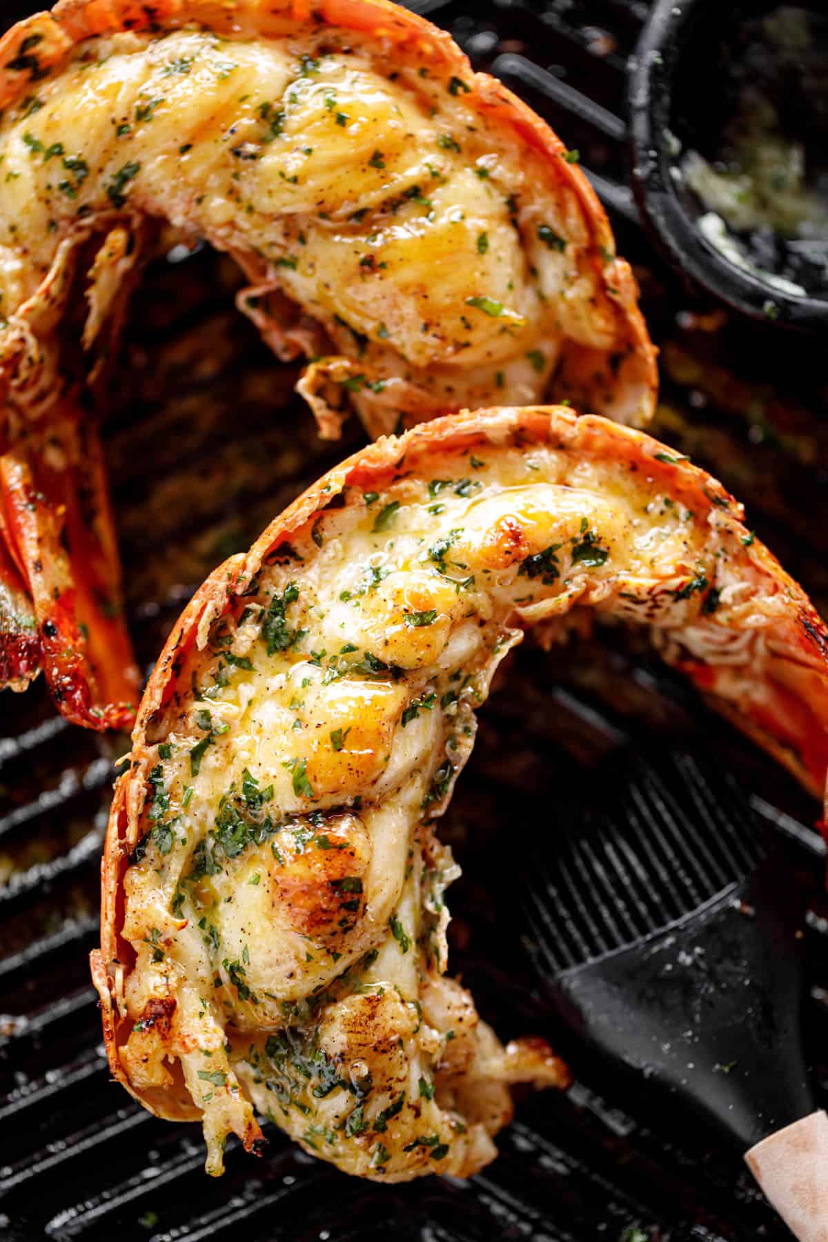 Grilled Lobster Tails garnished with melted garlic herb butter on a black grill pan.