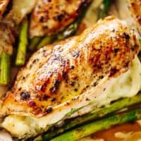Four asparagus and mozzarella cheese stuffed chicken breasts in a white casserole dish.