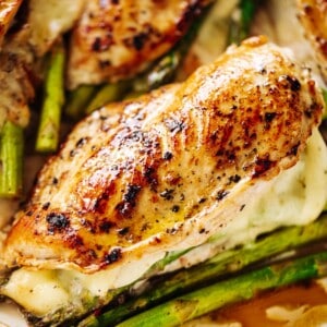 Four asparagus and mozzarella cheese stuffed chicken breasts in a white casserole dish.