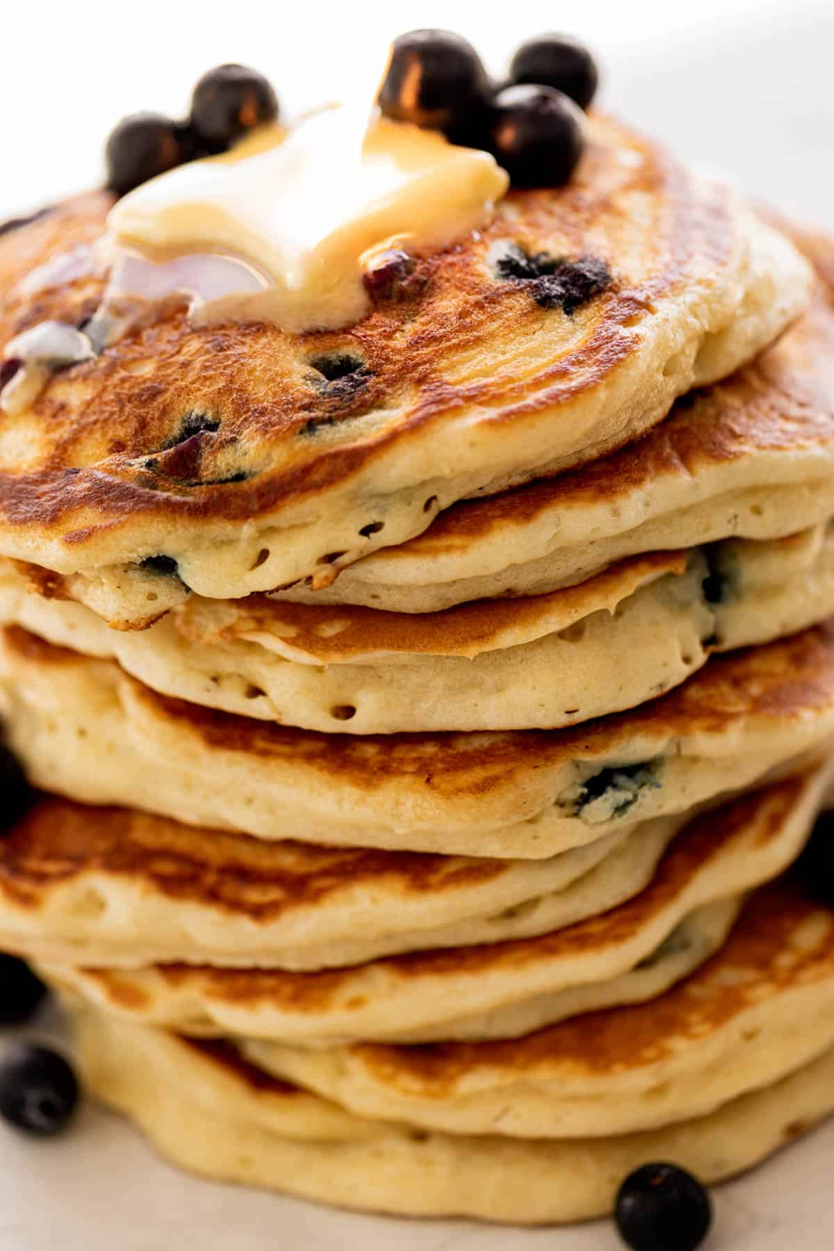 Ide view image of a stack of Blueberry Pancakes on a plate topped with fresh blueberries and melted butter.