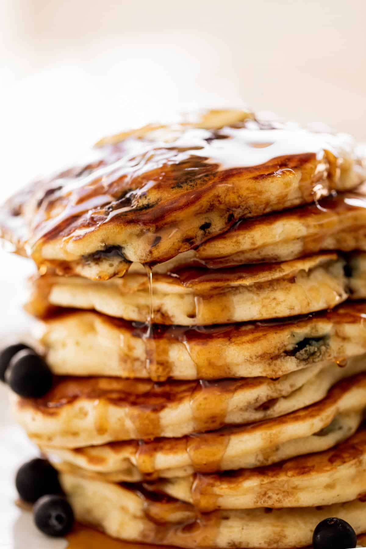 Topped with fresh blueberries. A stack of Blueberry Pancakes on a plate with maple syrup.