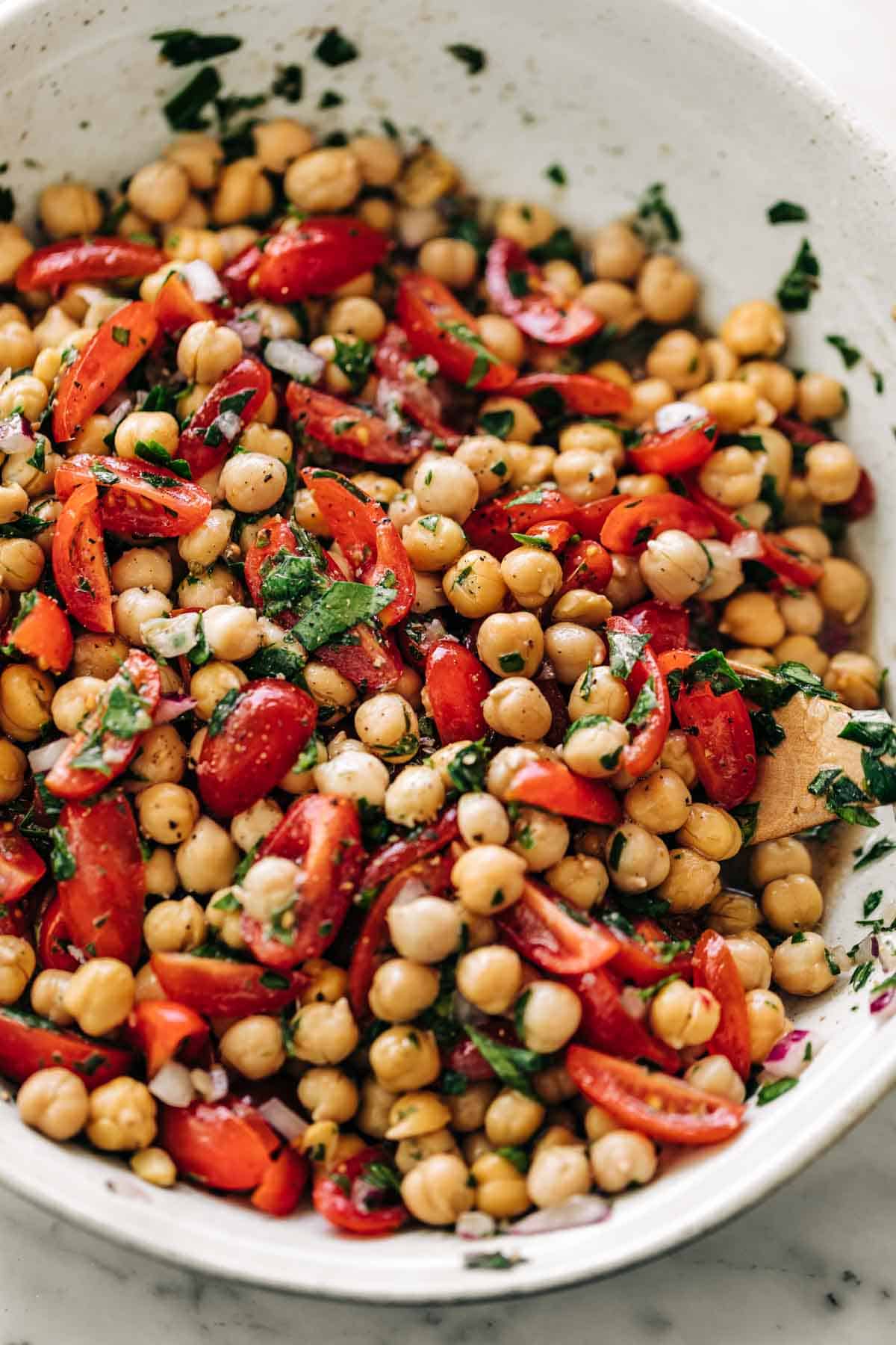 Chickpea Tomato Salad mixed with a lemon herb dressing in a white bowl on a white marble table background.
