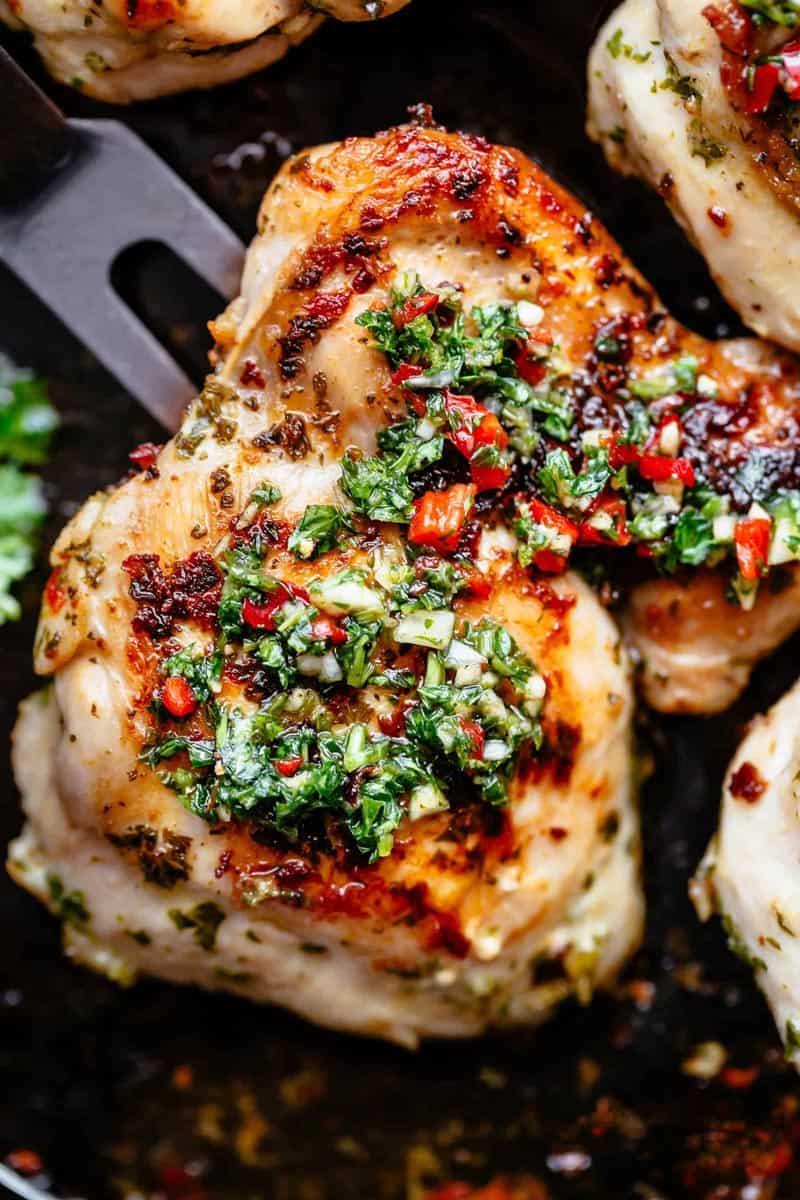 Golden roasted chicken on a black pan, topped with Chimichurri.