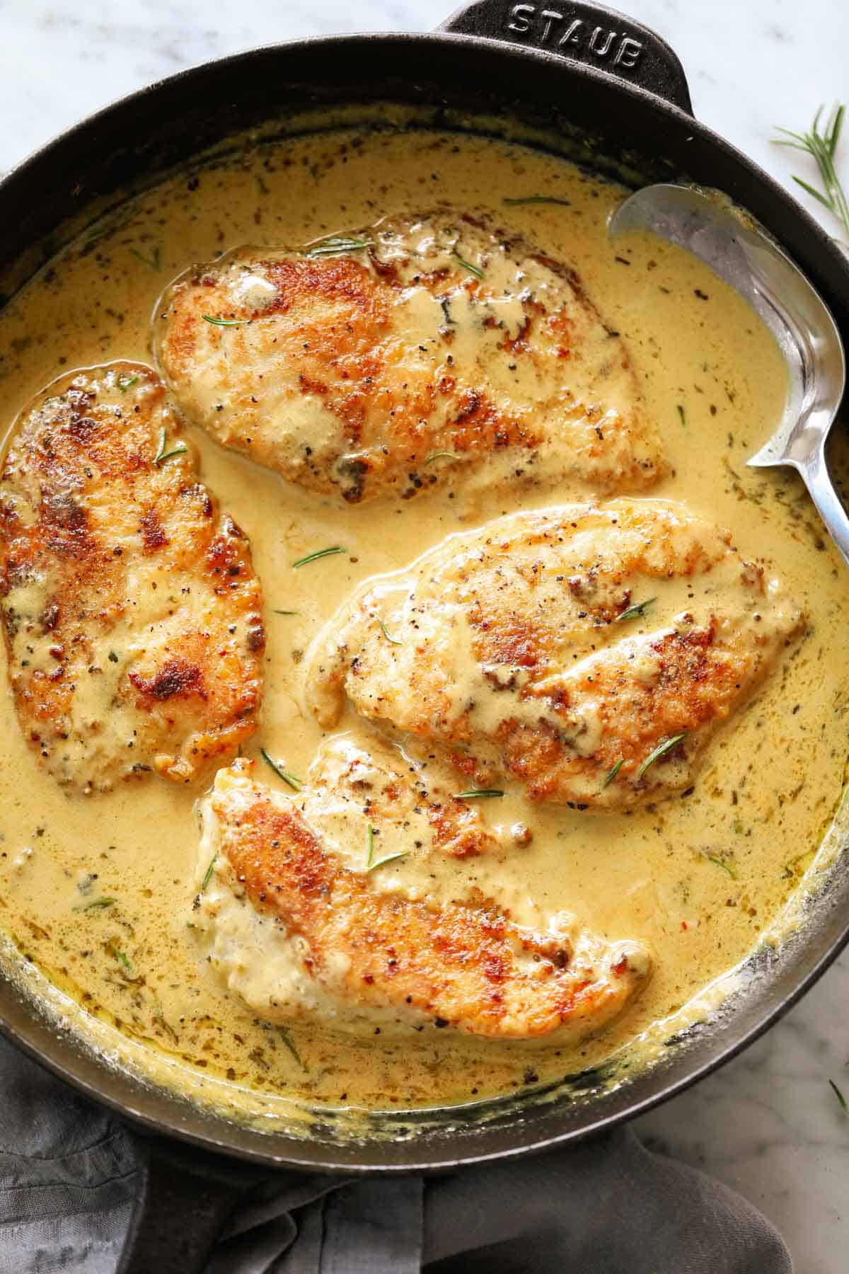 Creamy mustard chicken breasts in a black Staub skillet with a metal spoon.