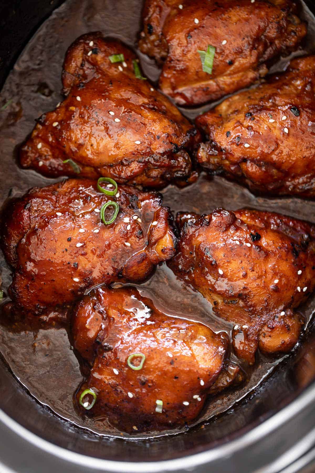 Delicious Boneless skinless chicken thighs in a black slow cooker bowl cooked till brown and coated in honey garlic sauce.  