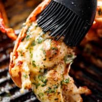 Grilled Lobster Tails brushed with melted garlic herb butter on a black grill pan.