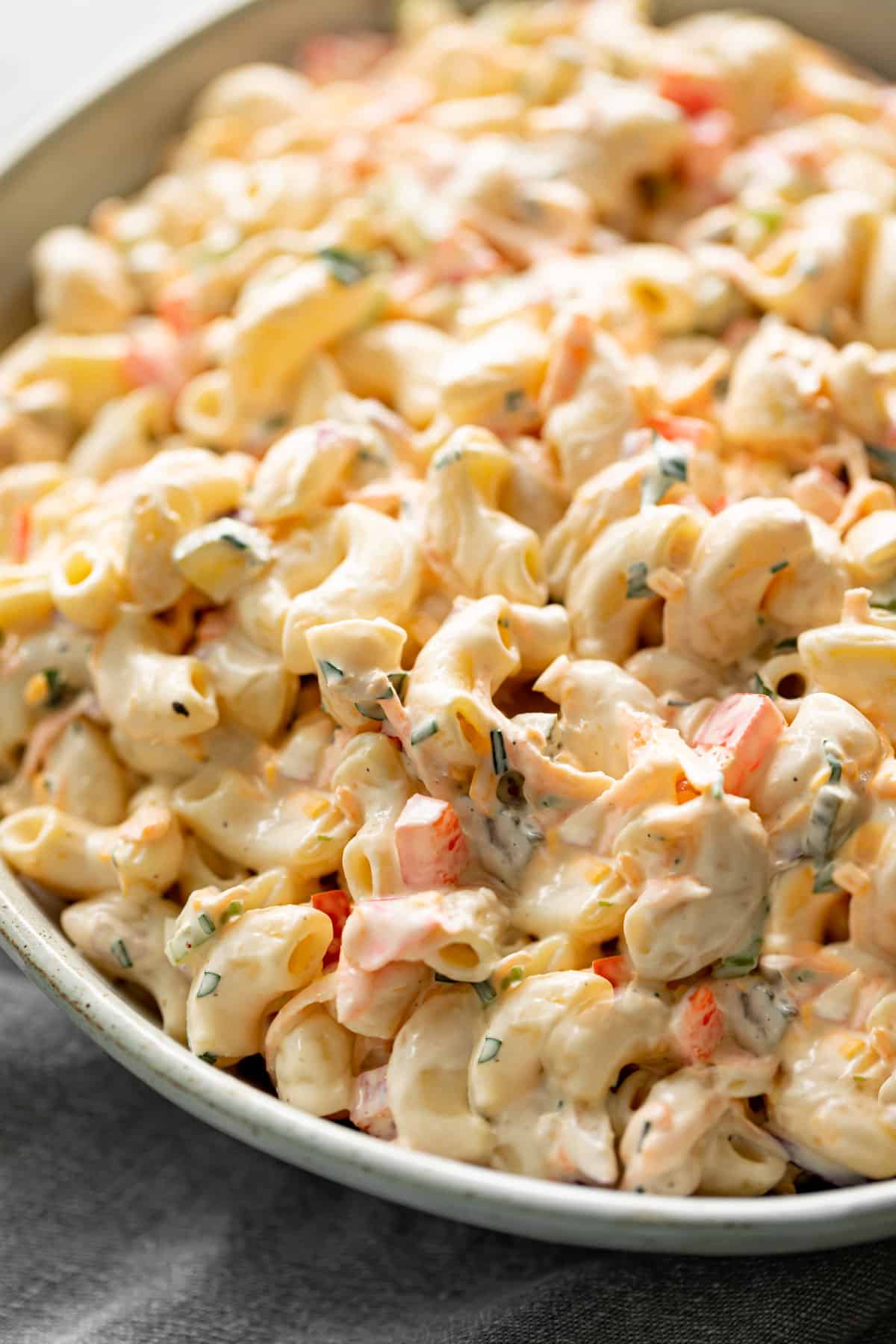 With a delicious creamy mayo dressing and fresh ingredients, A super creamy macaroni salad is so easy and quick to make! You\'ll love this recipe! Served in a light grey bowl on a grey linen cloth.
