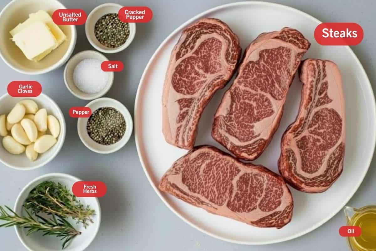 Flat lay photo of ingredient shot of steaks, unsalted butter, crushed pepper, salt, pepper, fresh herbs, garlic cloves, oil