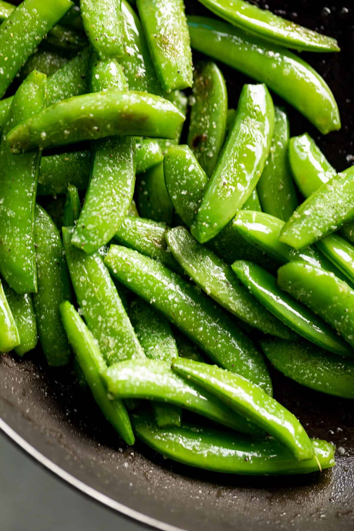 Top view of Sauteed Snap Peas in a black pan, sprinkled with coarse salt.