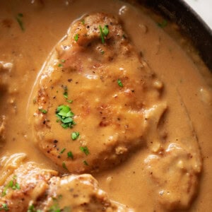 Smothered Pork Chops cooked in a black skillet garnished with fresh chopped parsley.