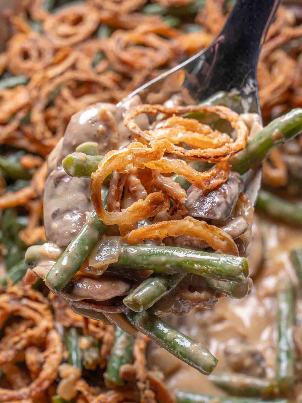 spoon full of green bean casserole being held above the dish