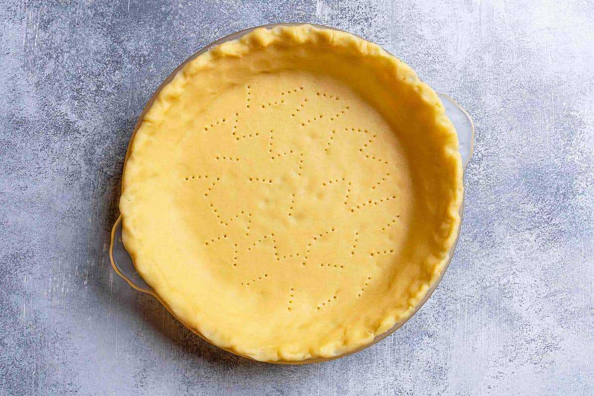 A pierced homemade pie crust base, perfectly laid in a baking dish, ready for the next delicious layer.