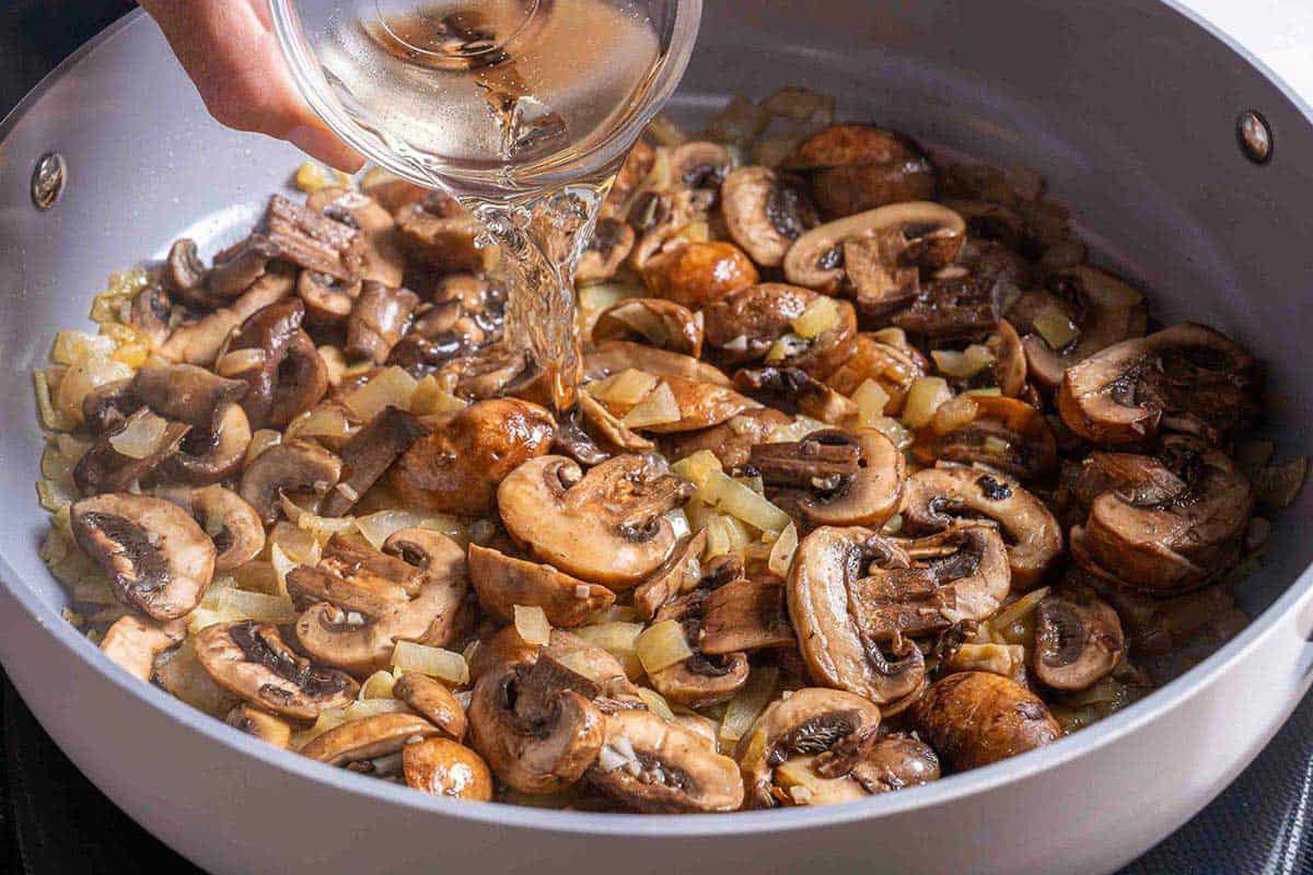 wine being poured into pan of mushroom soup