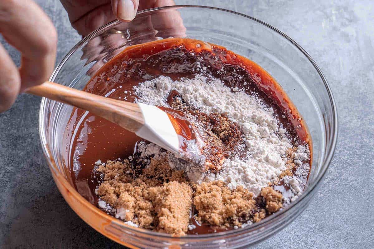 Melted dark chocolate, butter, eggs, corn syrup, brown sugar, and vanilla being mixed in a clear bowl.