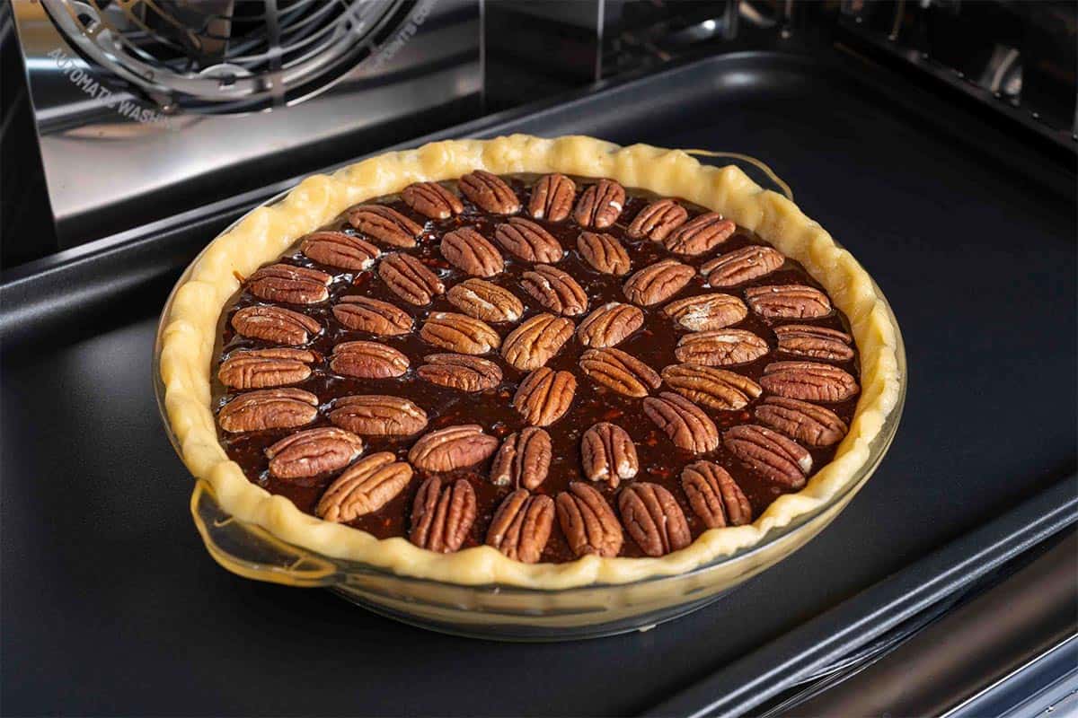 Pecan pie topped with pecans, baking in the oven.