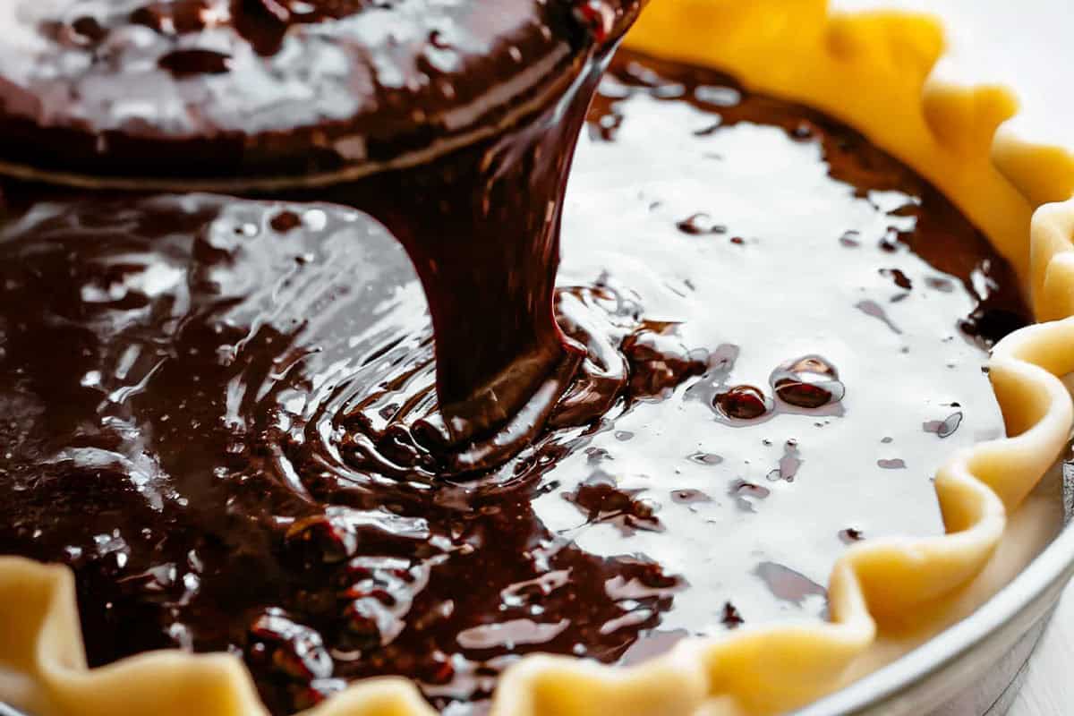 Gooey chocolate pecan mixture being poured into a homemade pie crust.