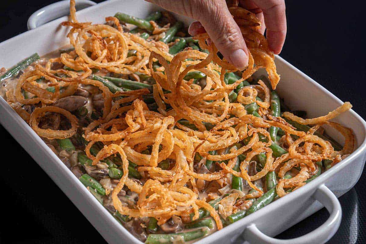 green bean casserole in a baking dish being topper with fried onion rings