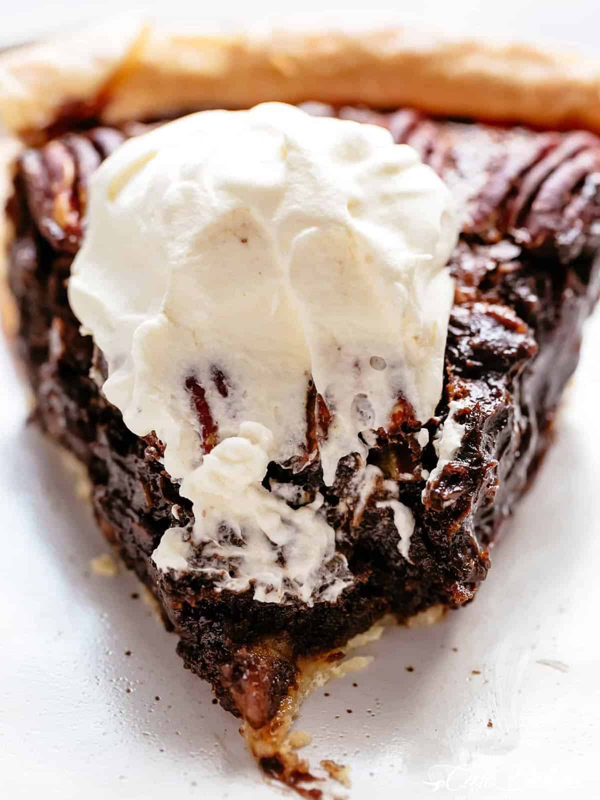An image of a chocolate pecan pie with a dollop of cream on top, with the point cut.