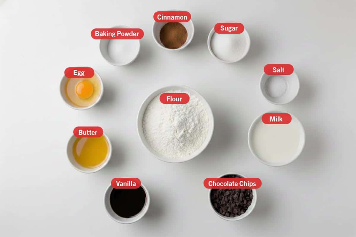Top shot of ingredients: vanilla, butter, egg, baking powder, cinnamon, sugar, salt, milk, chocolate chips, and flour.