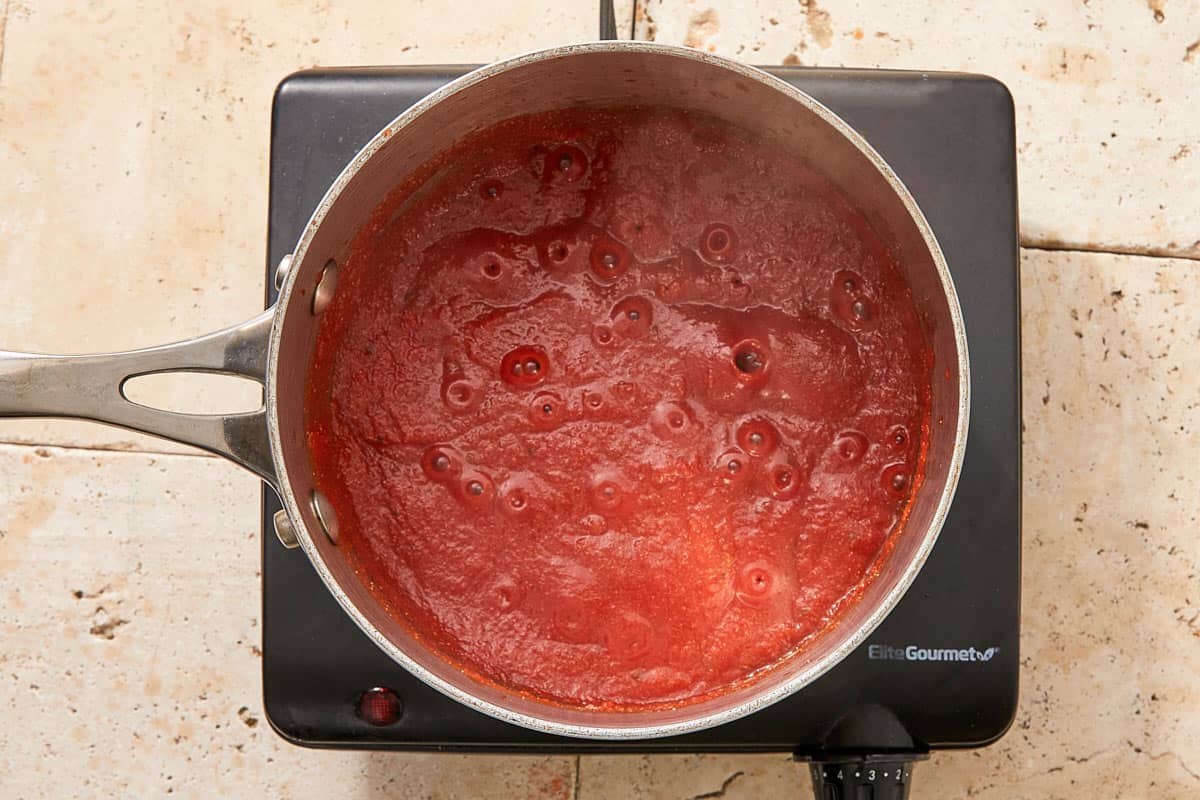 Tomato sauce bubbling in a saucepan on a black portable stovetop.