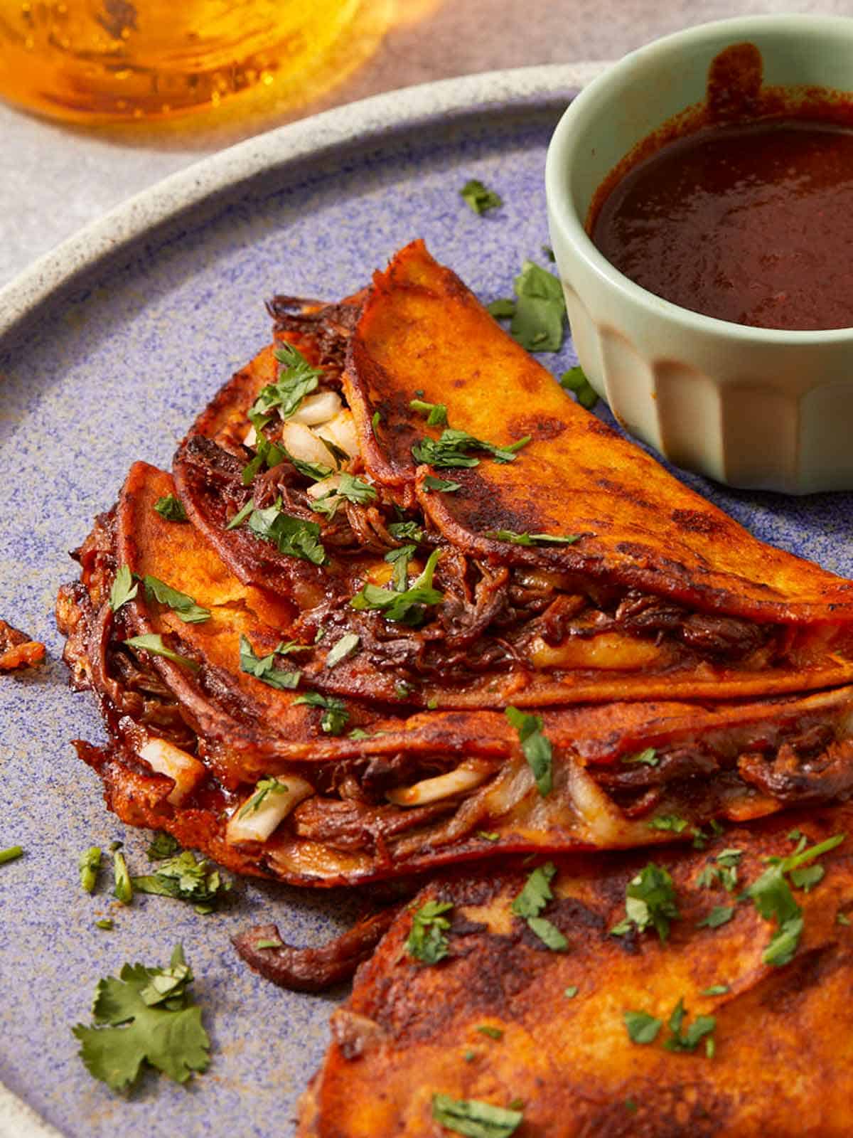 Close-up of crispy birria tacos served with consommé.